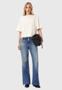 Lichtbeige cropped t-shirt met kanten rand, gecombineerd met hooggetailleerde, uitlopende blauwe denim jeans. Zwarte handtas met gouden accenten.