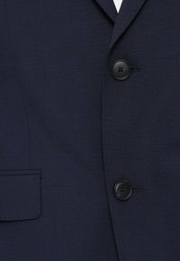 Στρατιωτικού μπλε σακάκι με υφή, δύο μαύρους κουμπιά και μία τσέπη. Κλασικός σχεδιασμός με κομψή εφαρμογή και δομημένα πέτα.