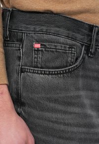 Grijze spijkerbroek met een duidelijke textuur, voorzien van een rood label op het voorzakje en gedetailleerde stiksels langs de naden.