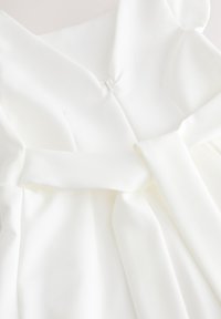 Vêtement en tissu blanc avec un col en V profond et une ceinture assortie nouée à la taille.