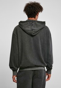 Felpa oversize grigia scura con una finitura texturizzata, dotata di cappuccio con coulisse e polsini a costine. Tessuto simile a un maglione, design casual.