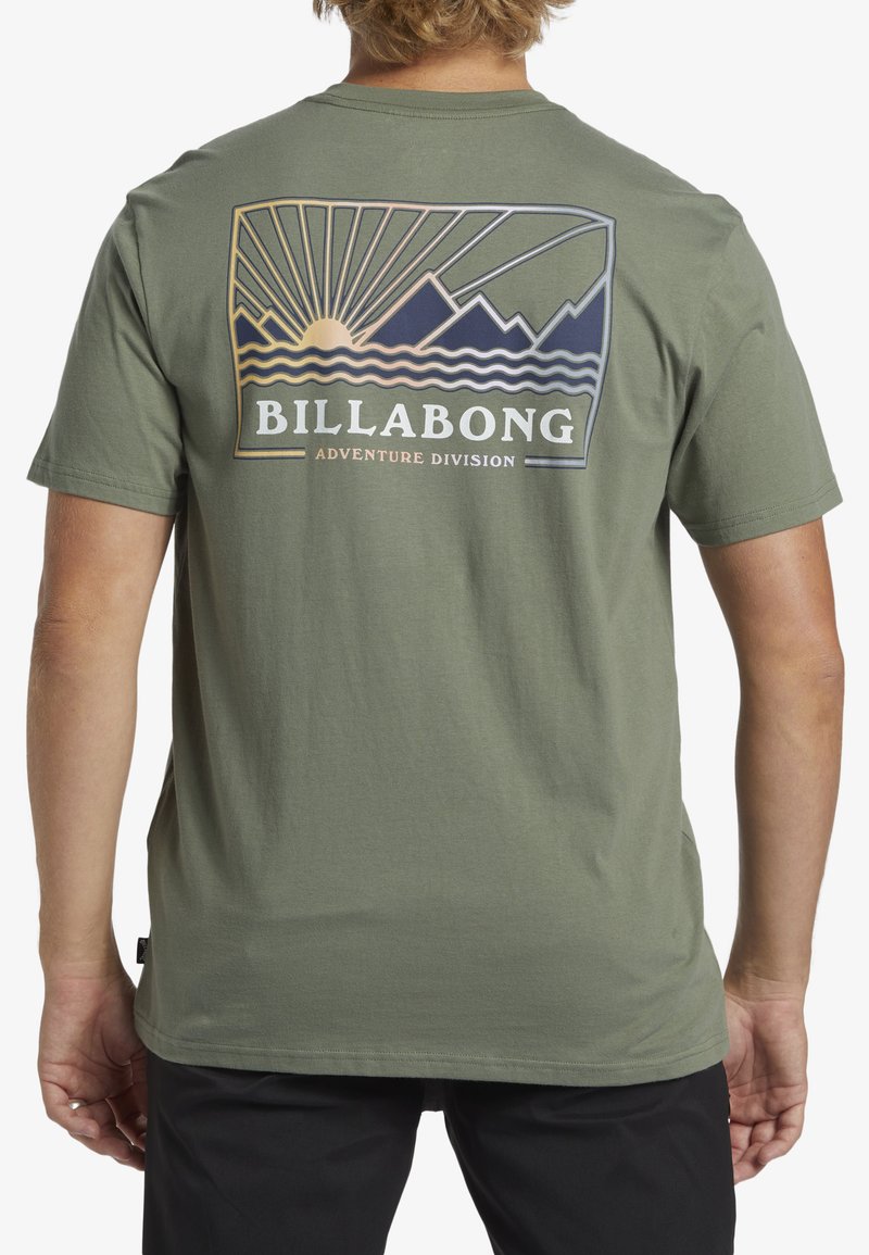 Olive green t-shirt made of cotton with a graphic print on the back featuring mountains, sunrays, waves, and the text "BILLABONG ADVENTURE DIVISION."