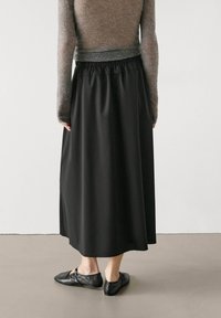 Gonna nera lunga fino alla caviglia con una superficie liscia e vita elastica, abbinata a un maglione grigio aderente a maniche lunghe e ballerine nere.