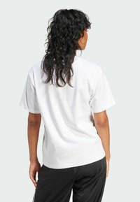 Camiseta blanca de algodón de manga corta, con un corte relajado y una textura suave, combinada con pantalones deportivos negros. Vista desde atrás.