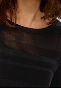 Haut à manches longues rayé noir avec un col rond. Le matériau semble doux et légèrement transparent, montrant un motif texturé.