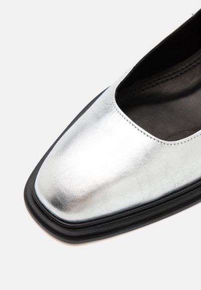 Hõbedane metallik king, millel on läikiv nahkviimistlus, neljakandiline varvas ja must kummitald. Õmbluste detailid ülaviilu ääres.