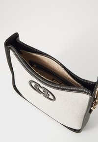 Torebka z płótna i skóry w białym i czarnym kolorze, z zamkiem błyskawicznym, złotymi elementami oraz wyraźnym logo z przodu. Wnętrze w kolorze beżowym.