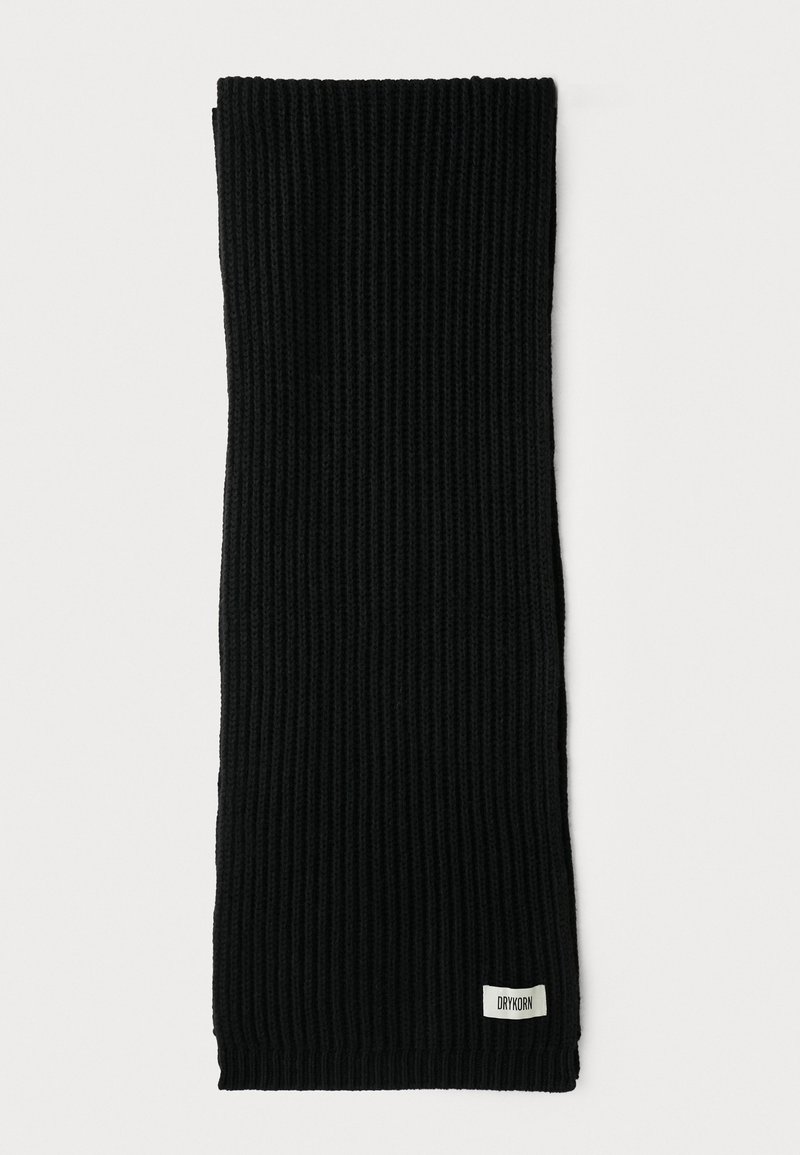 Sort ribbet strikscarf med et lille hvidt rektangulært mærke syet nær bunden på en hvid baggrund.