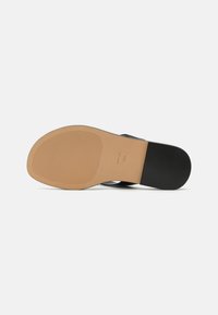 Scarpa nera con suola testurizzata; presenta una suola esterna marrone chiaro e una tomaia liscia. Il design include dettagli minimi e una forma elegante.