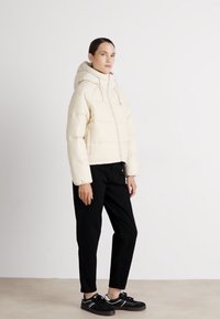 Cream puffer jacket with a hood, featuring quilted sections, paired with black pants and black sneakers with white accents.