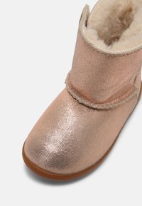 Bottine scintillante marron clair pour tout-petit avec doublure en laine douce, coutures visibles et semelle en caoutchouc marron sur fond blanc.