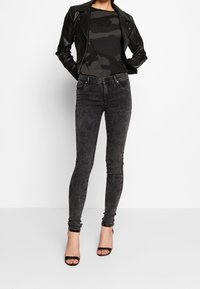 Černá koženka přes top s maskáčovým vzorem, zkombinovaná s tmavě šedými skinny džíny a černými sandály na tenkých podpatcích.