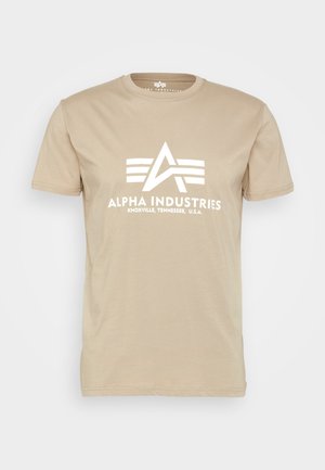 Camiseta de algodón beige con un gráfico blanco en la parte frontal que incluye el texto "ALPHA INDUSTRIES" y un logotipo triangular. Mangas cortas, diseño de cuello redondo.