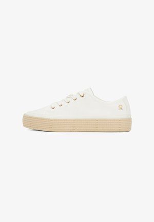 Sneaker bianca in tela con suola beige simile a una corda, orecchini dorati e un piccolo logo sul tallone. Design a basso profilo con punta arrotondata.
