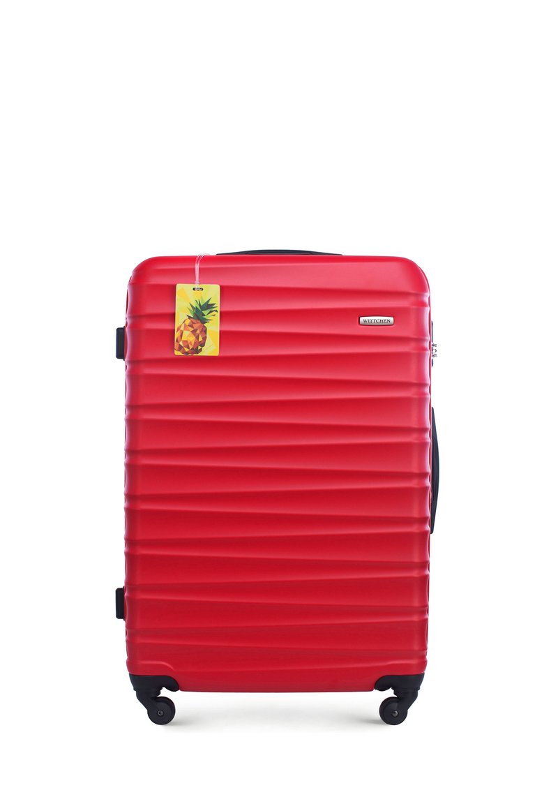 Valise rigide rouge avec un design rainuré, roues noires et une poignée supérieure. Comprend une étiquette de prix sur le thème de l'ananas attachée.