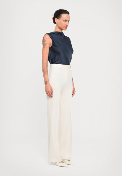 Navy sleeveless top with draped design, paired with high-waisted white wide-leg pants and pointed toe white shoes. Smooth fabric texture.