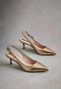 Gold metallic slingback heels with pointed toes, a low heel, and a bow accent on the back strap. Smooth texture and minimalistic design.