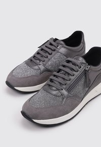 Sneaker grigie caratterizzate da un mix di materiali lisci e testurizzati, tra cui pelle scamosciata e dettagli metallici, con lacci anteriori e una zip laterale.