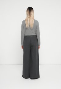 Grauer, gerippter Pullover mit langen Ärmeln, kombiniert mit weit geschnittenen, grauen Hosen, die eine glatte Textur und Gesäßtaschen haben.