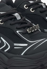 Czarne buty sportowe z siateczki i syntetycznej poszycia, odblaskowe srebrne akcenty, okrągłe sznurówki oraz dekoracyjny, przypominający kryształ, detal na języku.