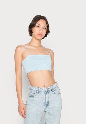 Top cropped azul claro feito de tecido elástico, com alças finas tipo espaguete e uma textura suave. Combinado com jeans de cintura alta.