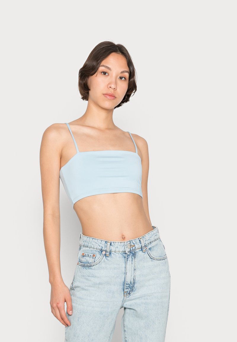 Top cropped azul claro feito de tecido elástico, com alças finas tipo espaguete e uma textura suave. Combinado com jeans de cintura alta.