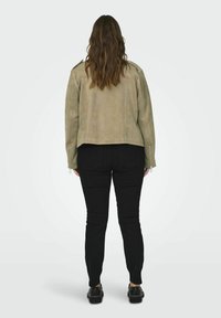 Chaqueta de motocicleta de ante en beige claro con un diseño corto, que presenta puños con cremallera. Combinada con jeans ajustados negros y zapatos negros.