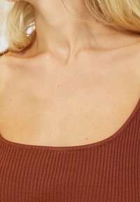 Débardeur marron à côtes avec un grand col rond. Le tissu a une texture lisse et une coupe ajustée, idéale pour le superposition.