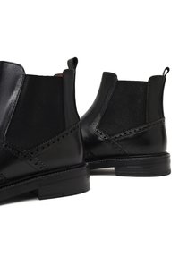 Botas Chelsea de cuero negro con paneles laterales elásticos, detalles de brogue y suelas de goma texturizadas. Incluyen tiradores para poner y quitar fácilmente.
