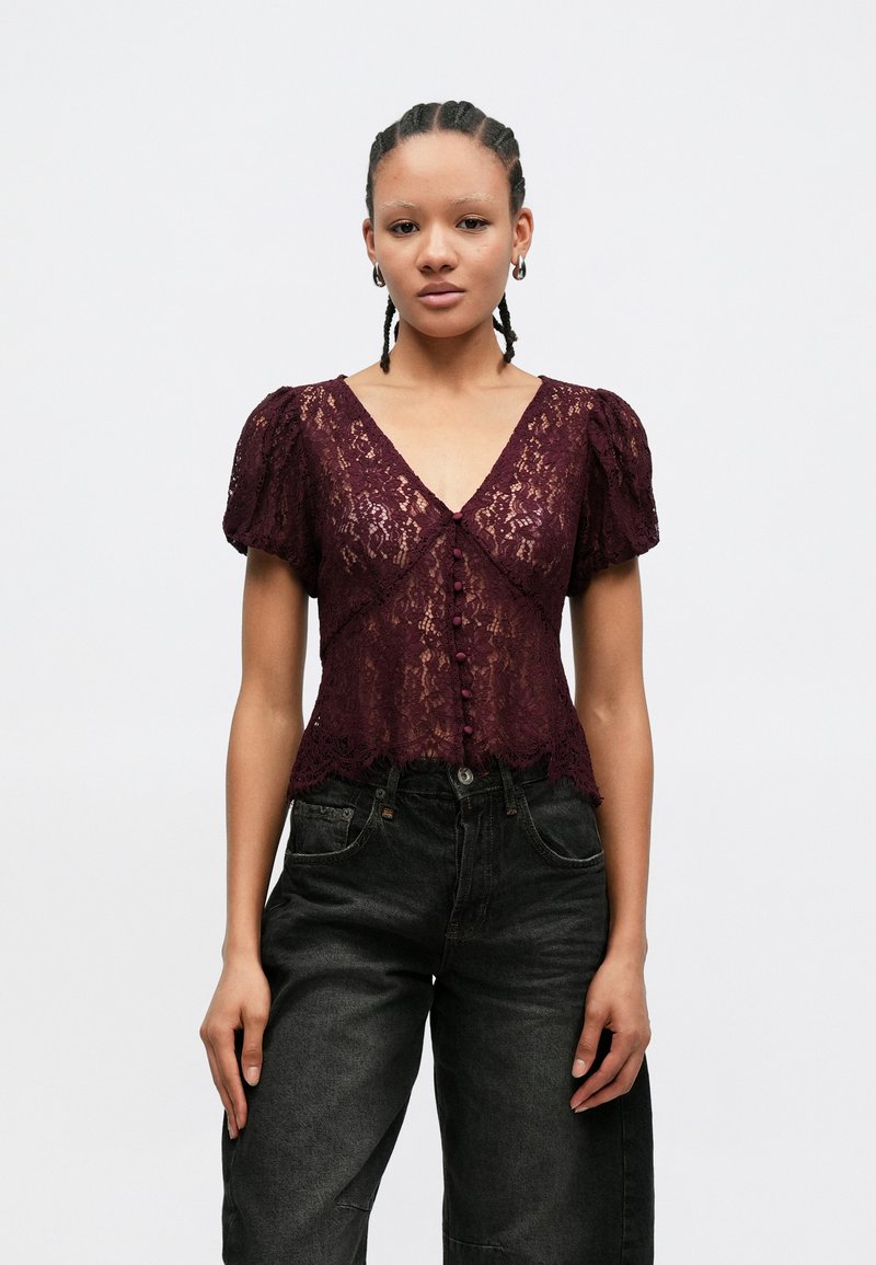 Blusa de renda borgonha com decote em V, mangas bufantes e bainha escalopeada. Apresenta botões decorativos na frente e padrões florais intrincados.