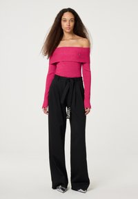 Strakoff-the-shoulder top in felroze brei, gecombineerd met hoge zwarte wijde broek met een decoratieve detail aan de zoom.