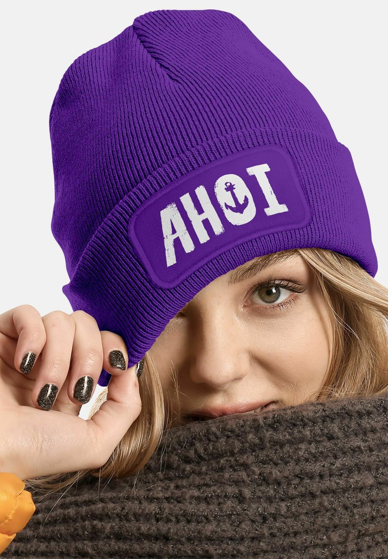 Purple knitted beanie featuring an embroidered "AHOI" patch with an anchor design. The fabric has a ribbed texture and a snug fit.