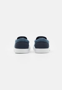 Blauwe stoffen sneakers met een donkerblauwe hielkap en witte rubberen zolen. Kenmerkt zich door een low-top ontwerp en een gewatteerde kraag voor comfort.