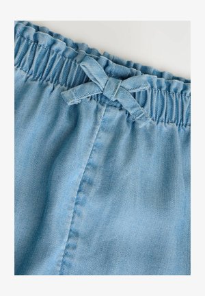 Pantalones cortos de denim azul claro con una cintura elástica con volantes y un detalle de lazo de tela. Textura suave con detalles de costura sutiles.