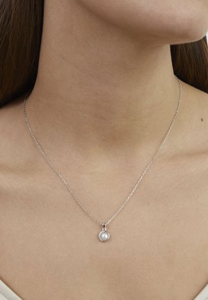 Sølvkæde med et rundt vedhæng, der har en central perle omgivet af små klare sten. Glat tekstur, delikat design.