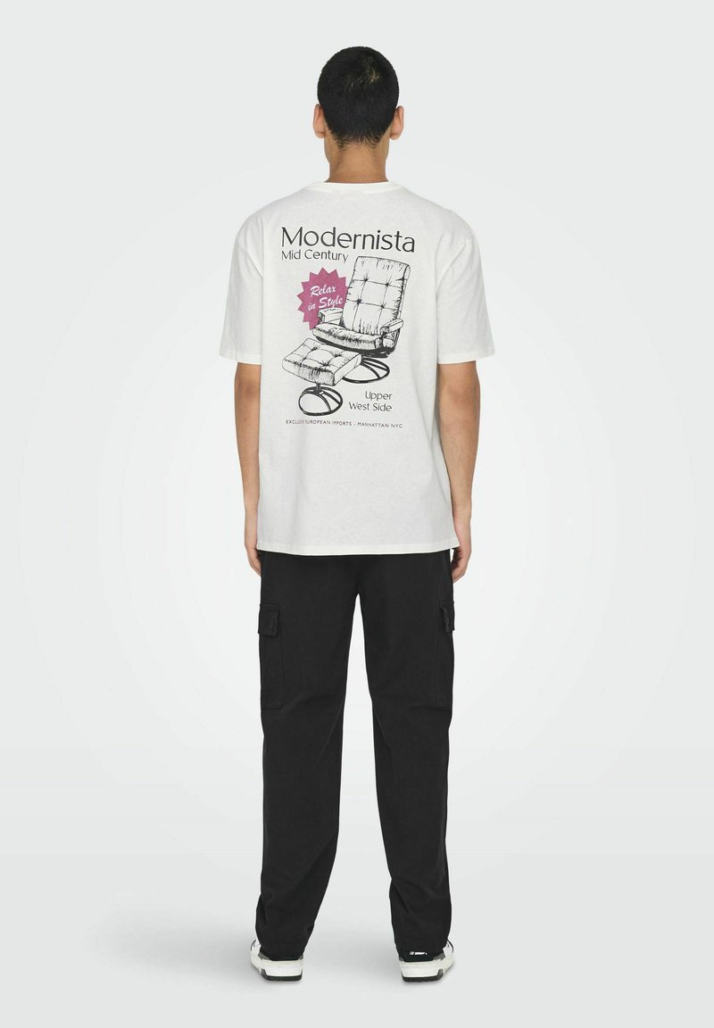 T-shirt blanc avec un motif au dos représentant un design de chaise des années 50, texte noir et accents roses. Pantalons cargo noirs et baskets blanches visibles.