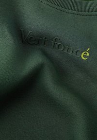 Tissu vert foncé avec un texte noir en relief "Vert foncé" et la dernière lettre "é" en jaune près du centre supérieur.