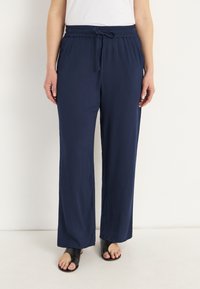 Marineblauwe broek met wijde pijpen van een textiel met structuur, voorzien van een elastische tailleband en verstelbaar trekkoord. G gedragen met zwarte instapsandalen.