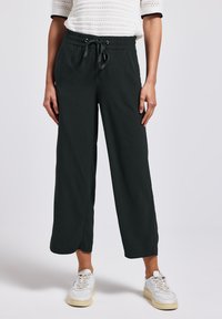 Černé kalhoty s širokými nohavicemi, elastickým pasem a šňůrkou, s hladkou texturou látky a bočními kapsami. V páru s bílými teniskami.