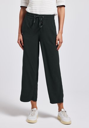 Pantalones de pierna ancha negros con cintura elástica y cordón, con una textura de tela suave y bolsillos laterales. Combinados con zapatillas blancas.