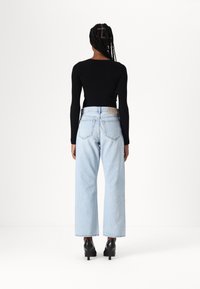 Top negro de manga larga con ribetes, combinado con jeans de pierna ancha de color azul claro, que presentan un detalle en el bolsillo trasero y zapatos de tacón negros.