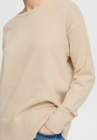 Maglione beige con scollatura rotonda e polsini a coste. Realizzato in morbido tessuto a maglia, presenta una vestibilità rilassata e spacchi laterali per il massimo comfort.
