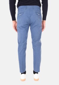 Chinos in cotone blu con una vestibilità dritta, dotati di tasche posteriori con bottone e texture sottile. Abbinati a scarpe da ginnastica bianche e calzini neri.