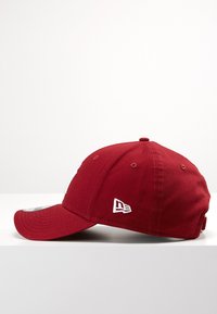 Piros baseball sapka ívelt peremmel, puha anyagból készült. Oldalán fehér hímzett logó és szellőzőlyukak találhatók.