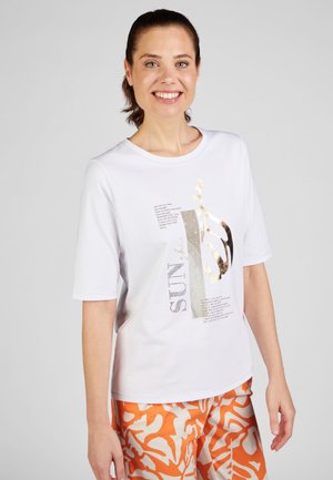White short-sleeve t-shirt with printed text and decorative accents. Paired with orange patterned shorts. Smooth fabric texture.