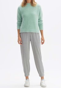 Pull en tricot pelucheux vert menthe à manches trois-quarts, associé à un pantalon gris clair effilé avec deux poches avant, et des baskets blanches.