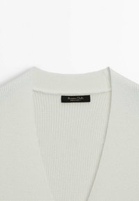 Cardigan bianco a coste con un design a V profonda. Presenta una texture morbida e un'etichetta che recita "Massimo Dutti" all'interno del colletto.
