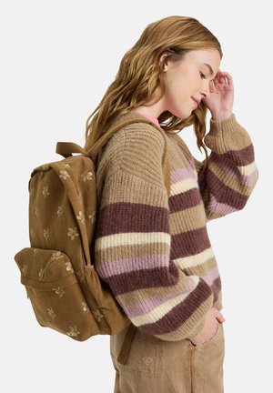 Brown corduroy backpack with floral embroidery and two front pockets, worn by a person in a striped sweater, featuring shades of beige and purple.