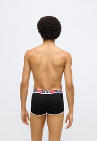 Boxeri negri cu margini albe și o talie elastică de marcă inscripționată cu „DIESEL” în roșu și negru. Modelul este prezentat din spate.