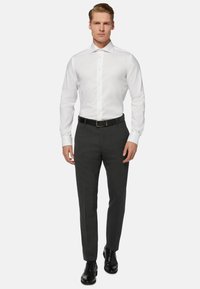 Camicia bianca con colletto a punta, cintura nera, pantaloni formali grigio scuro e scarpe nere, che presentano un look aderente e un tessuto morbido.